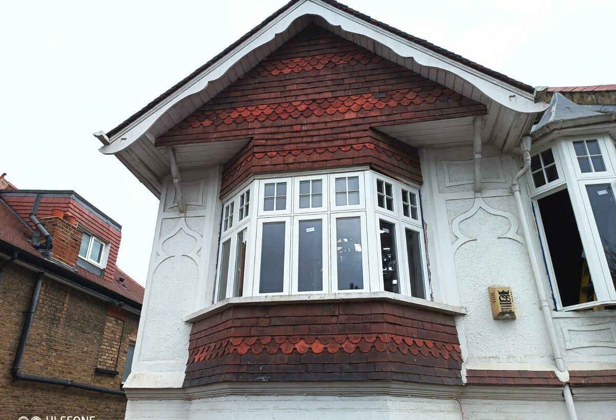 Restored timber casement bay windows on an Arts and Crafts house with tile-hung gable