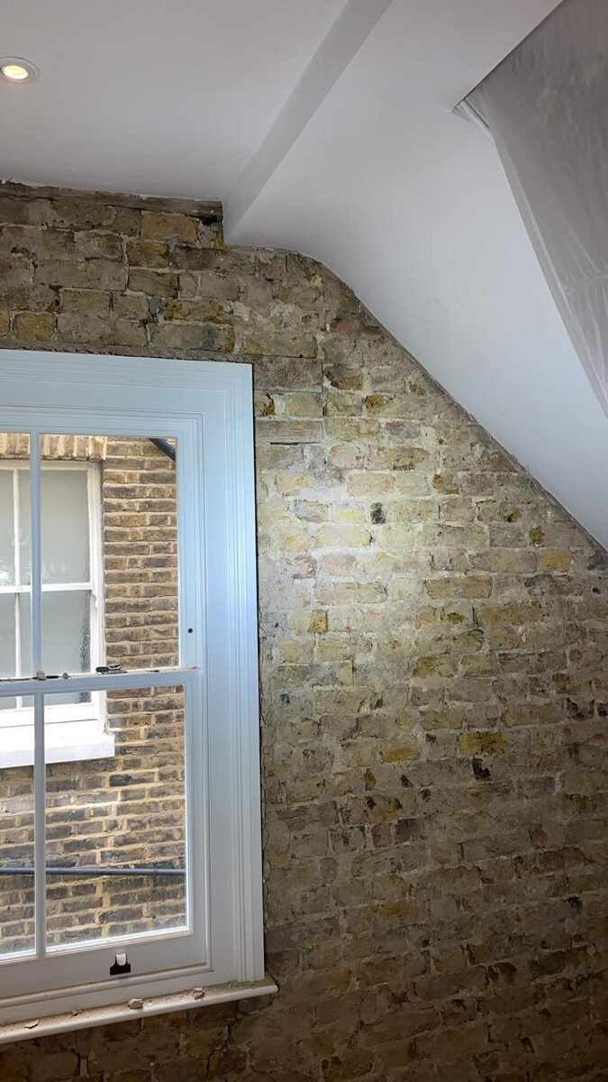 Pale blue timber sash window against exposed brick in a loft conversion