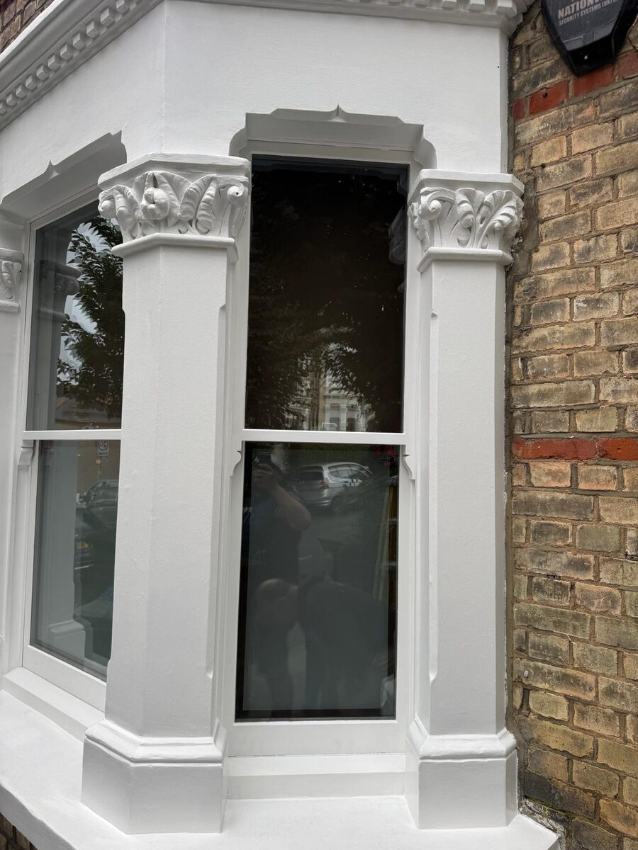 Restored timber bay sash windows with ornate stucco columns on a Victorian terrace