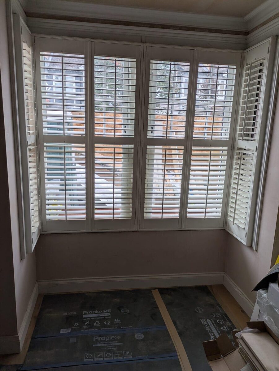 Square bay timber windows fitted with white plantation shutters during a refurbishment